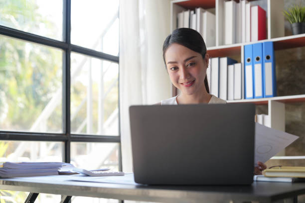istock Asian Businesswoman Using laptop computer and working at office with calculator document on desk, doing planning analyzing the financial report, business plan investment, finance analysis concept. 1455534470