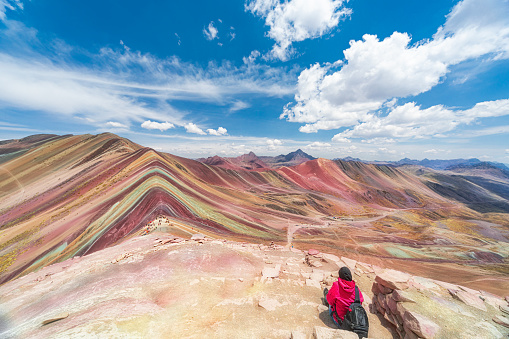 Female tourist sits in the foreground of the Rainbow Mountains at an altitude of 5000 meters.