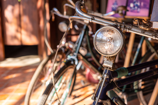 Close up on bike headlight with blurry background of other vintage and old bikes inside antique shop.