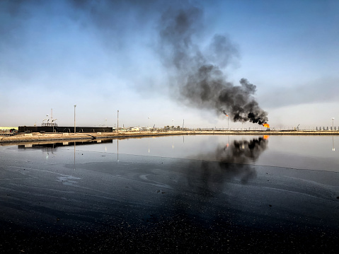 Oil fields in Iraq, Fluent pit with mixed water and crude oil and black smoke in the background