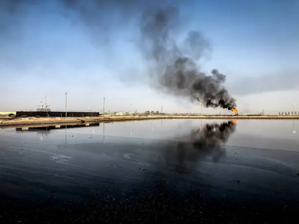 Oil fields in Iraq, Fluent pit with mixed water and crude oil and black smoke in the background