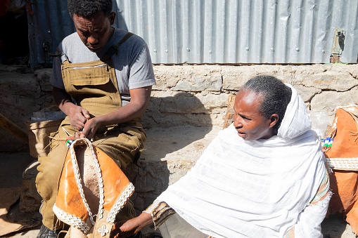 Old woman and her son sitting on the street working with leather in Ethiopia. Embroidery and designs on the leather bags.