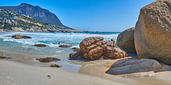 A small wave feathers and breaks at Long Beach, in Kommetjie, Cape Town, with the mountains of Table Mountain National Park in the background.