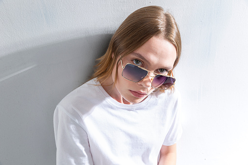 Blonde freckled girl wearing sunglasses. Photo studio with sunlight.