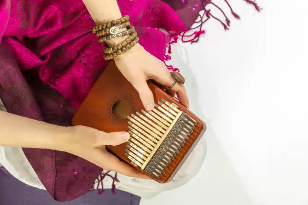 Woman holding kalimba in her hands and playing. Concept of Relaxing at home, Me time and self care and sound meditation. Woman enjoy the melodious sound of the thumb piano playing. Closeup