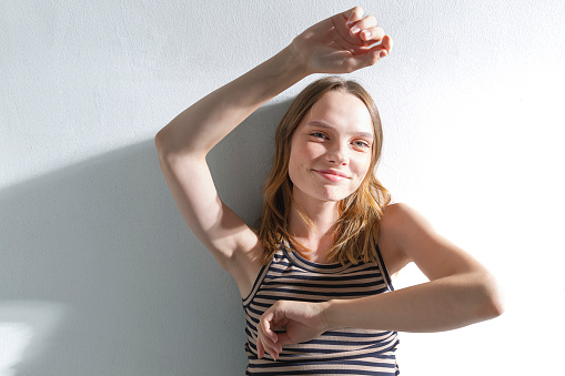 A blonde and freckled girl on a white background, wearing a striped brown t-shirt. Studio with sunlight.