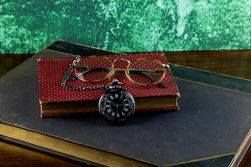 Old Books with Pocket Watch and Spectacles on a Wooden Table Top