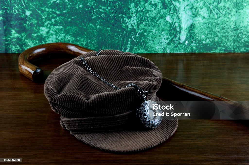 Corduroy Hat with Walking Stick and Pocket Watch on a Varnished Table Top Walking stick with pocket watch and corduroy hat on a wooden surface Antique Stock Photo