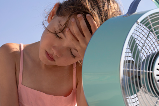 Little girl cools down with fan during the summer heat.