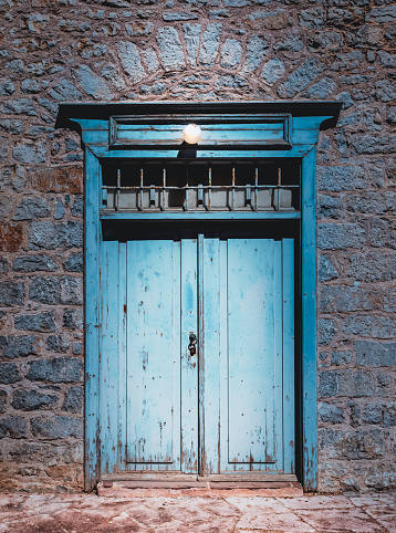 Front view of blue double wooden door lit by a lamp above. Old architecture in Hydra town, Greece.