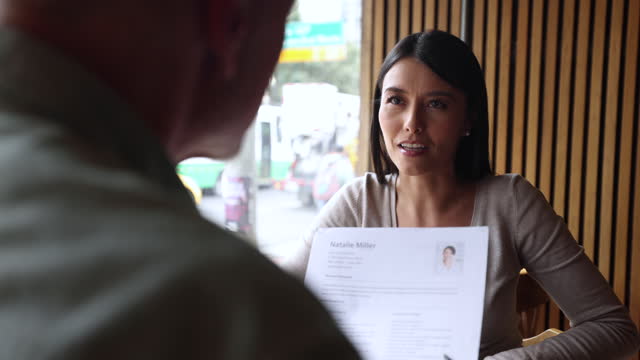 Unrecognizable businessman interviewing a beautiful woman at a coffee shop while looking at her resume