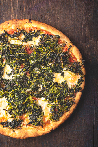 Neapolitan Italian pizza with wild broccoli or turnip greens or Friarielli ( broccoletti  Romani, broccoli di rapa in Calabria, cime di rapa in Puglia ), smoked provola cheese on a wooden  rustic background. Regional  green pizza