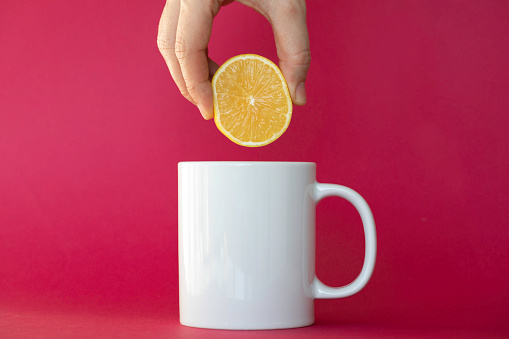 Hand Squeezing Lemon into tea cup, red background.