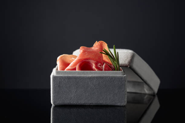 Prosciutto with rosemary in a gray gift box on a black background.