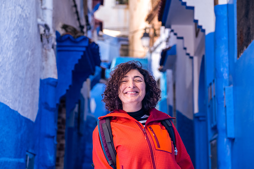 An adventurous adult female traveler, traveling alone, walks the streets of a picturesque village with blue painted houses. Some people prefer to travel alone to travel at a more leisurely pace.