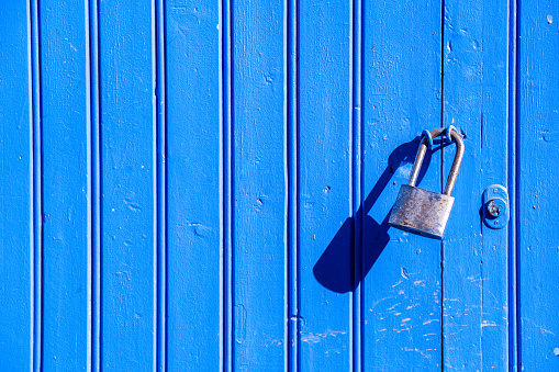 Blue wooden background with vertical lines and a rusty steel padlock.