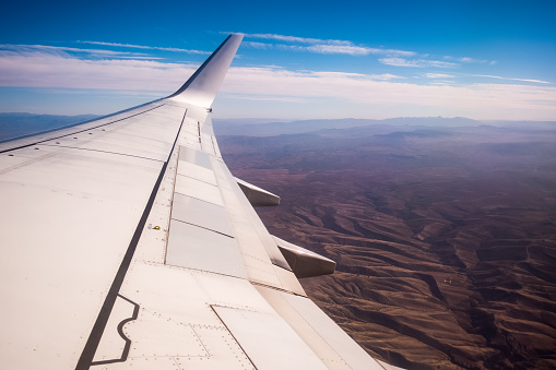 Right wing of an aircraft in flight taken from inside the aircraft. A mountainous ground can be seen below. For some people flying is an anxious, stressful and anxious time.