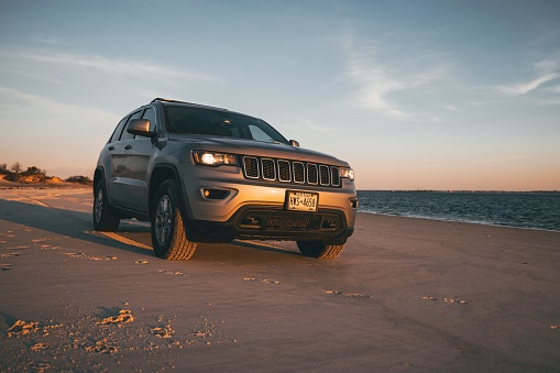 Fire Island, United States – January 01, 2023: A gray 2018 Jeep Grand Cherokee at the beach at sunset