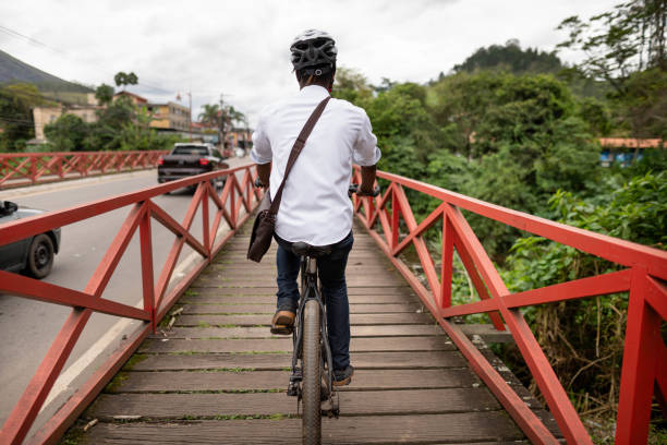 Rear view of a man wearing a helmet riding a bicycle across a bridge during his commute to work