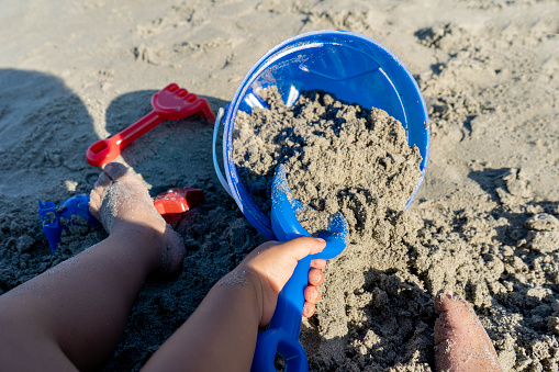 A child plays in the sand with a yellow shovel. Summer time. Children's toys on the beach