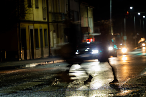 City street night blurred background. Dark dressed pedestrians crossing the street at night.. Bokeh night city life. The city of Ustrzyki Dolne, Poland.