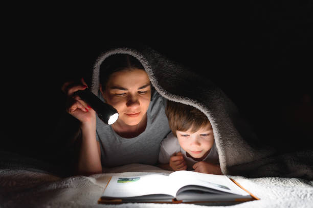 istock Family Mom and little son reading a book with a flashlight under the blanket. 1455562140