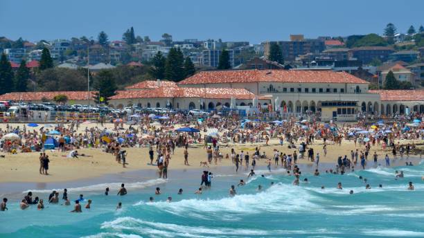 Iconic Bondi Beach in Sydney on hot clear sunny day with the famous bathing pavilion in the background and many swimmers in the turquoise water Bondi is a popular spot with young beachgoers bondi junction stock pictures, royalty-free photos & images