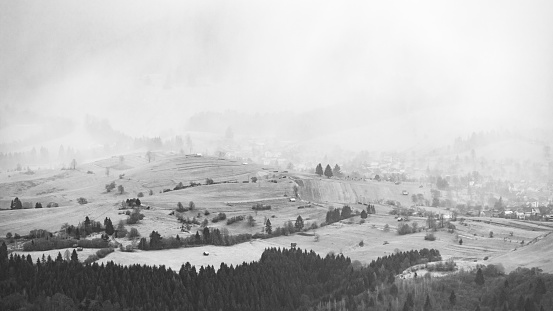 A grayscale shot of a landscape of many mountains in foggy weather.