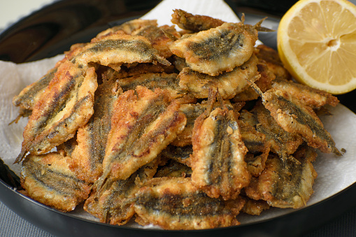 Pan fried anchovy fish in a plate with lemon on the side
