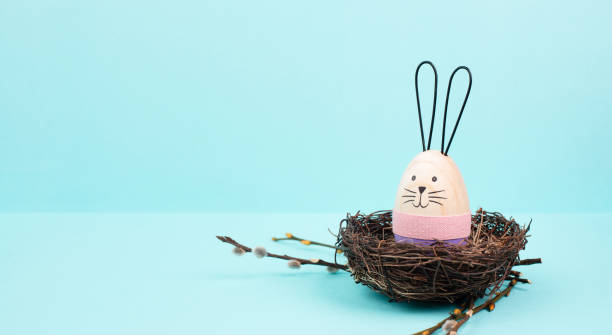 istock Easter bunny or rabbit sitting in a bird nest, willow branches, wooden egg, spring holiday, brown and blue color 1455574458