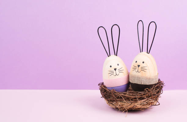 Easter bunny or rabbit couple cuddle together in a wicker nest, wooden egg, spring holiday greeting card