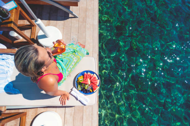 istock Woman drinking and Aperol Sritz sitting on a deck chair on a deck by the ocean. 1455576066