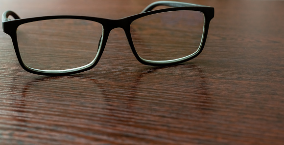 Stylish eyeglasses on office table close-up on blurred background