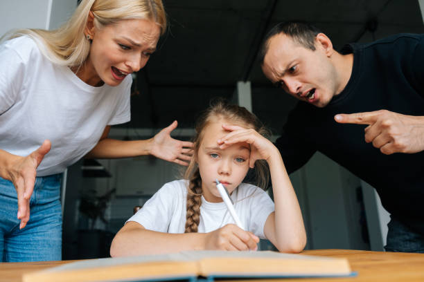 portrait of angry young parents yelling and scolding together lazy little daughter sitting at table, doing homework, sad looking at camera. - anger furious mother adult imagens e fotografias de stock