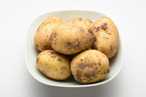 High angle view fresh organic raw potatoes in a bowl on white background
