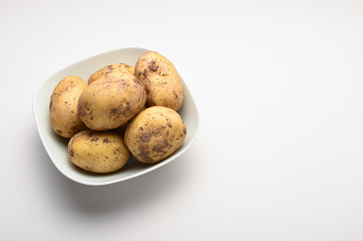 High angle view fresh organic raw potatoes in a bowl on white background with copy space