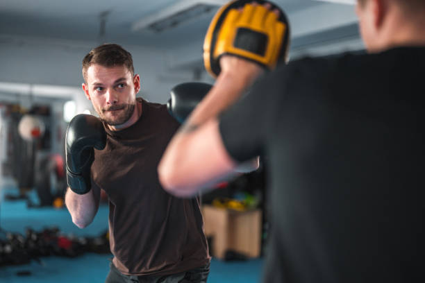 Caucasian Male Boxer Working Hard Caucasian male boxers practicing in a gym. Working hard on new boxing sequences. Sweating hard with a coach. boxing gym stock pictures, royalty-free photos & images