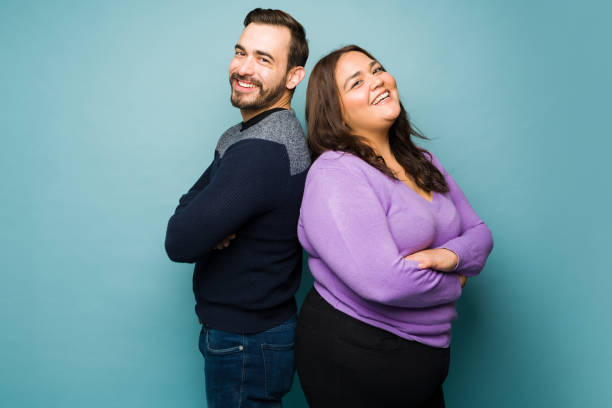 Fun attractive couple laughing together Excited beautiful young couple laughing and having fun together while dating against a studio background pudgy woman pictures stock pictures, royalty-free photos & images