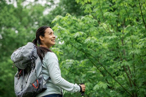Mature woman smiles while exploring nature and hiking with backpack and hiking poles