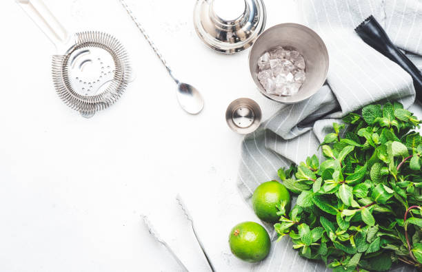 istock Mojito cocktail making. Mint, lime, ice - ingredients and steel bar tools. Top view, white table background, copy space 1455590224