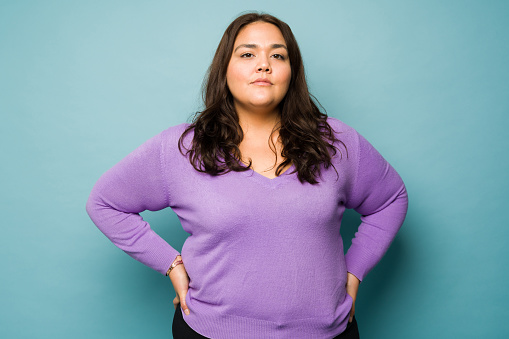 Serious overweight hispanic woman with her hands on the hips looking determined while making eye contact