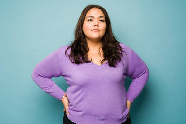 Somber fat woman looking at the camera Serious overweight hispanic woman with her hands on the hips looking determined while making eye contact serious photos stock pictures, royalty-free photos & images