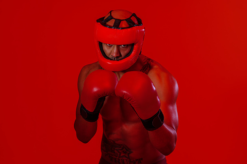 Man wearing head guard and boxing gloves practicing for fight on studio background