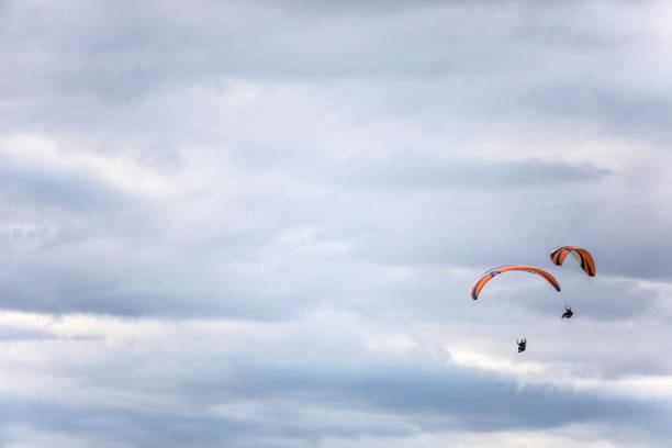 istock Paragliders flying, against a cloudy sky 1455593179