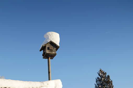 A wooden bird feeder covered in snow. This is where the birds are fed in winter.
