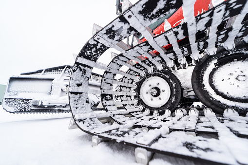 A large snow vehicle known as a snow caterpillar or snowcat with tank style tire tracks used to smooth out and groom ski runs.