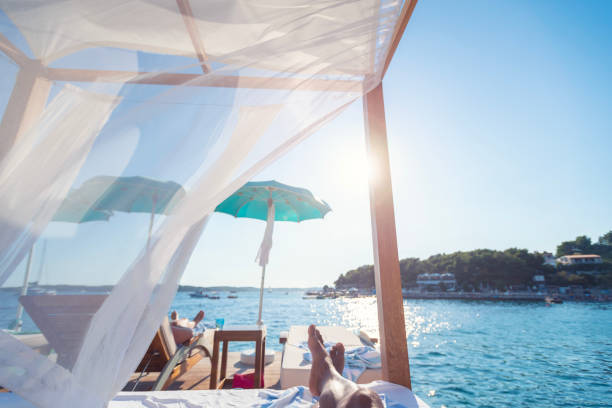 Man lying in a day bed at the beach. There is a see through curtain on the day bed. Water in the background