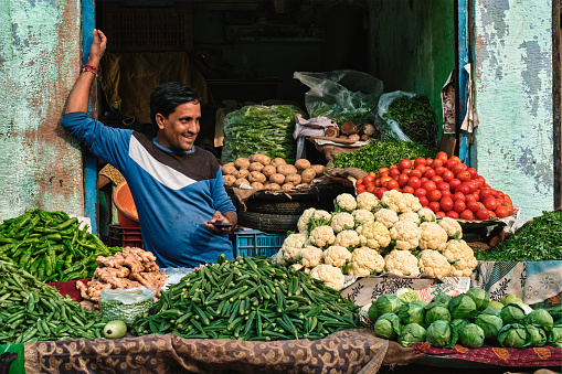 Jodhpur, India - November 14, 2019: Vegetable seller ih his shop in Sadar Market smiling and laughing. Jodhpur, Rajasthan, India