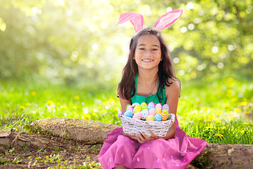 Easter egg hunt. Little girl with bunny ears celebrating Easter. Kids celebrate spring holiday. Children search chocolate eggs and candy. Rabbit costume. Christian holidays with child.