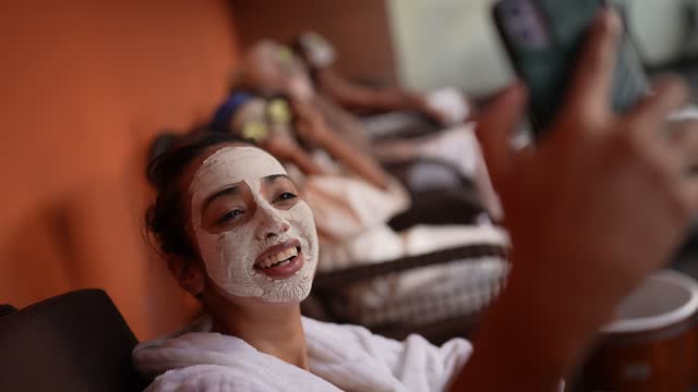 Women taking selfies on the mobile phone while using facial mask at a spa